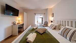 Habitació d'hotel amb llit, escriptori i cadira, televisió penjada a la paret i finestra amb cortines.
