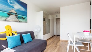 Una sala de estar moderna con un sofá gris, un ventilador blanco y un cuadro de una escena de playa.