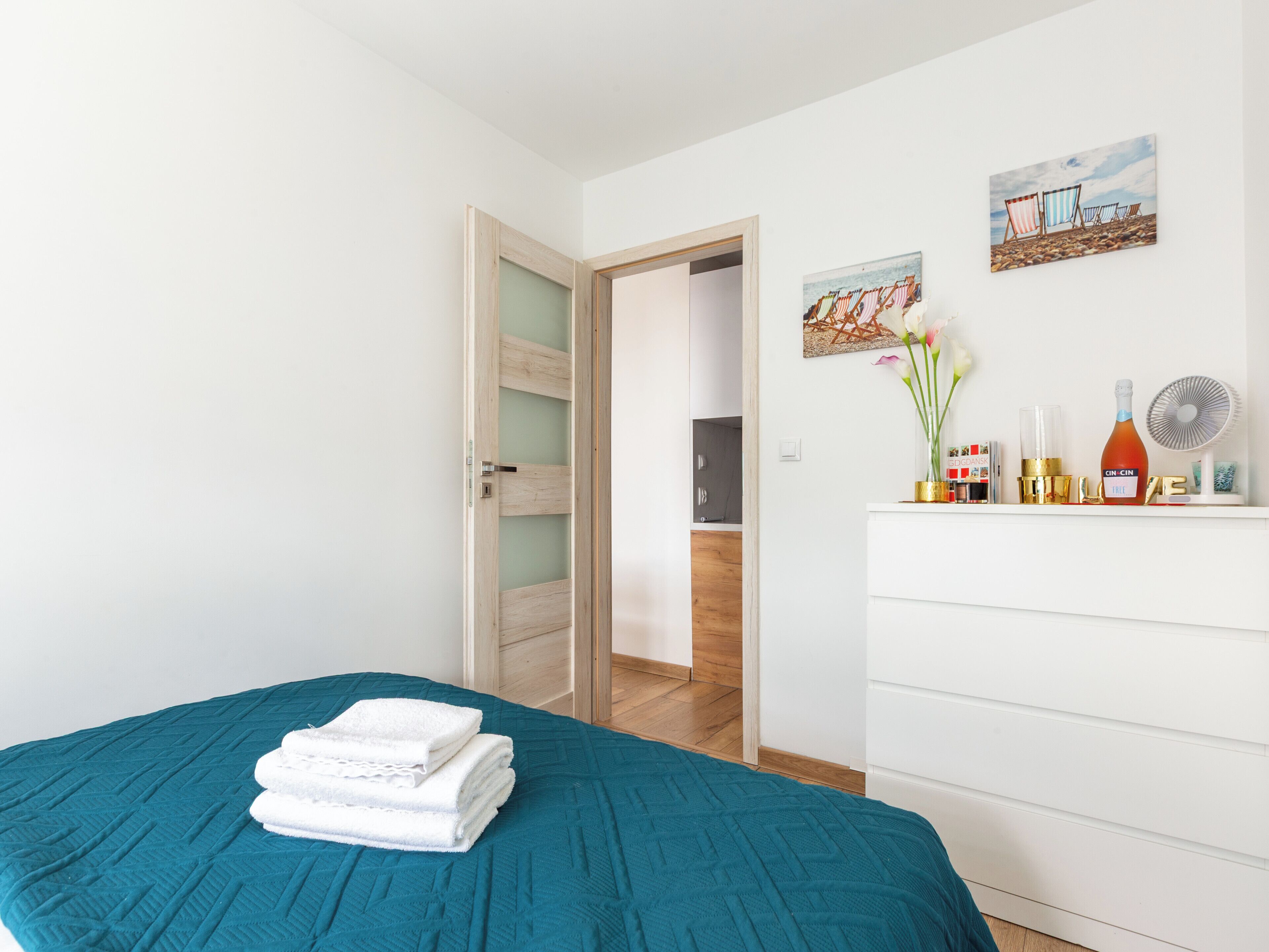 Un dormitorio con colcha color esmeralda, cómoda blanca y una puerta que da a otra habitación.