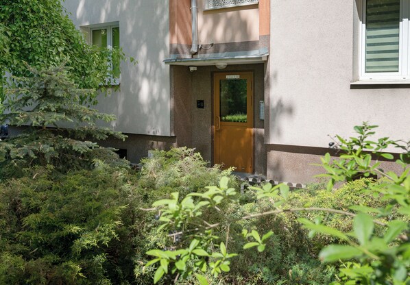 A building entrance with a wooden door, a small window, and a security camera above the door.