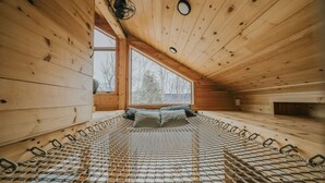 Een houten blokhut met hoge plafonds, een bed, een raam en een hanglamp.