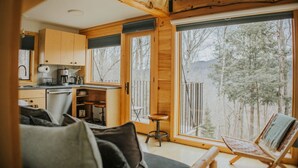 Een gezellig chaletinterieur met een keuken, eethoek en grote ramen met uitzicht op een bos.