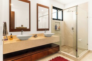 Une salle de bain moderne avec un grand miroir, deux lavabos et une douche à parois de verre.