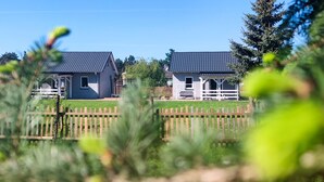 Two houses with dark roofs and white walls, separated by a wooden fence.