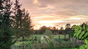 A garden with a wooden fence, trees, and a sunset in the background.