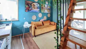 A room with a wooden floor, a sofa, a white chair, a small table, and a window with a view of bicycles.