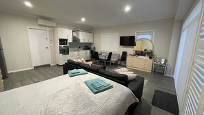 A modern apartment with a large bed, a sofa, a dining area, and a kitchenette. - 
Serene Getaway (Callala Beach)