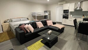 A modern, well-lit room with a bed, a sofa, a coffee table, and a kitchenette. - 
Serene Getaway (Callala Beach)