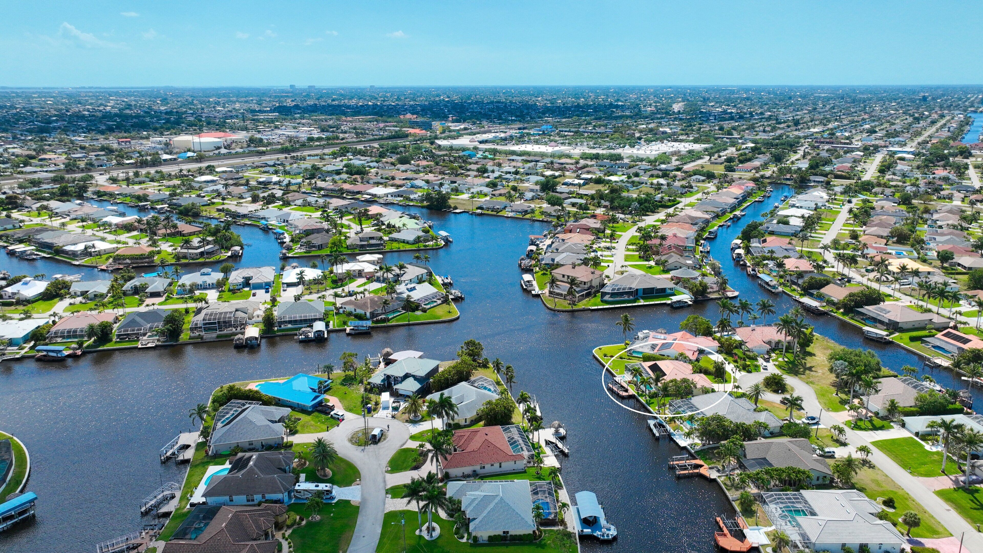 A residential area with houses arranged around a central waterway, featuring a mix of single and multi-story buildings, some with visible swimming pools.