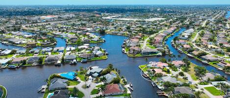 A residential area with houses arranged around a central waterway, featuring a mix of single and multi-story buildings, some with visible swimming pools.