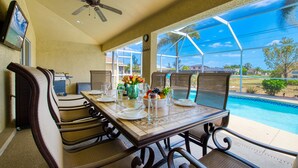 A dining area with a pool view, including a table set for four, chairs, and a ceiling fan. - VILLA SALTY ESCAPE - HEATED POOL | FAMILY FRIENDLY | BOAT RENTAL + TOURS VOUCHER INCL. (Cape Coral)