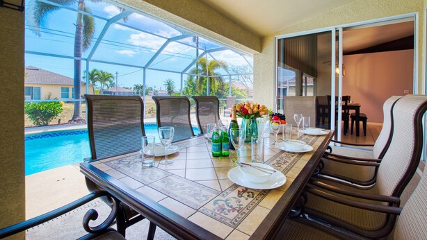 A dining area with a view of a swimming pool, outdoor seating, and a glass-enclosed patio. - VILLA SALTY ESCAPE - HEATED POOL | FAMILY FRIENDLY | BOAT RENTAL + TOURS VOUCHER INCL. (Cape Coral)