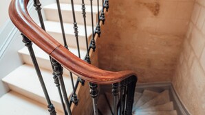 Une main courante en bois au design incurvé, une rambarde en métal noir et des marches de couleur beige.