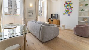 Un salon moderne avec une table en verre, un canapé gris et un téléviseur posé sur un meuble en bois.