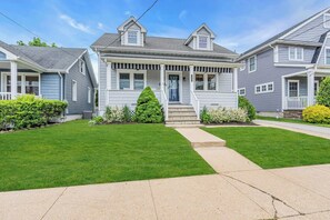 A two-story residential house with a front porch, a well-maintained lawn, and a driveway leading to the entrance.