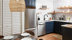 Une cuisine moderne avec un dosseret de carrelage blanc, des appareils en acier inoxydable, des étagères en bois et un coin repas avec une table dressée pour quatre personnes.