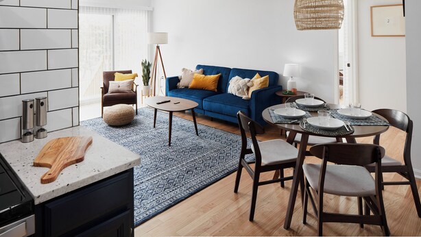 Une cuisine moderne avec une planche à découper en bois, un coin repas avec un canapé bleu et une table à manger dressée pour quatre personnes.