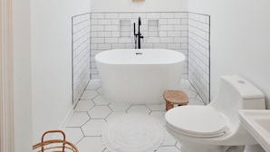 Une salle de bain avec une baignoire sur pieds, des toilettes et un petit tabouret en bois.