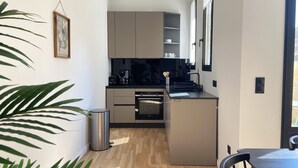 A compact kitchen with modern appliances, a trash bin, and a dining area with a table and chairs.