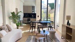 A modern living room with a sofa, a dining table with chairs, a coffee table, and a large window offering a view of the outside.