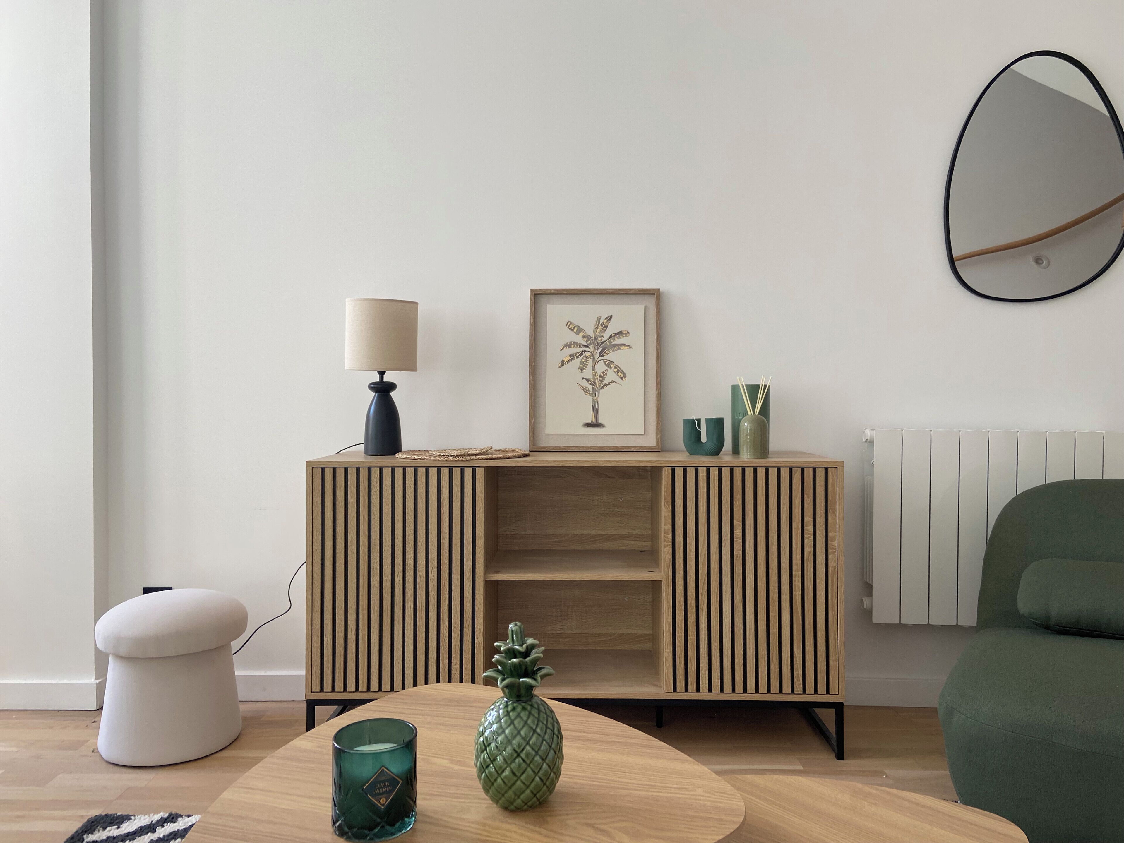 A modern living room with a wooden cabinet, a framed picture, a green pineapple vase, and a green chair.