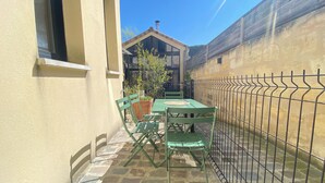 A small outdoor patio with a table and chairs, a potted plant, and a metal fence.
