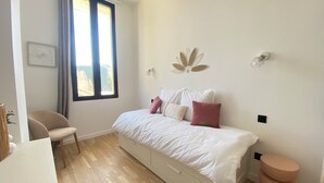 A bedroom with a bed, a chair, a window, and a wall-mounted light fixture.