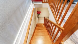 Una escalera de madera con barandilla que conduce a un rellano con un jarrón de flores rojas.