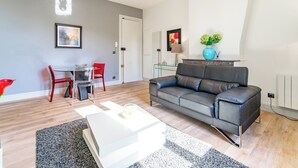 Una sala moderna con un sofá de cuero, una mesa de centro de vidrio y una zona de comedor con una silla roja y una mesa de vidrio.