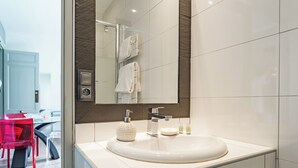Un baño moderno con un lavabo blanco, un espejo grande y una cabina de ducha de vidrio.