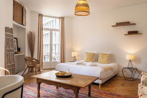 A bedroom with a bed, bedside tables, a chair, a table, and a window with curtains. - Charming Apartment for 4 in Downtown Bordeaux (Bordeaux)