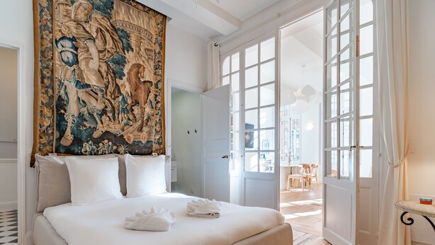 Une chambre spacieuse avec un grand lit, une tapisserie et une vue sur la ville, grâce à des portes ouvertes.