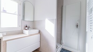 A bathroom with a window, a sink, a mirror, and a shower area.