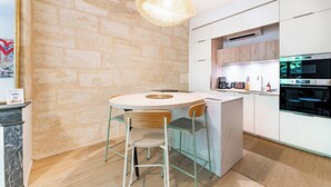 A modern kitchen with a round dining table, two chairs, a hanging light fixture, and built-in appliances.