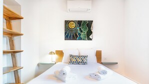 A hotel room with a bed, two nightstands, a wall-mounted air conditioner, and a wooden shelf unit.