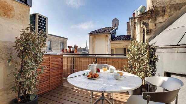 Une terrasse sur le toit avec une table ronde dressée pour le petit-déjeuner, entourée de plantes en pot.