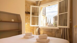 Une chambre d’hôtel avec un lit, deux serviettes, une fenêtre avec des rideaux et une vue sur des immeubles.