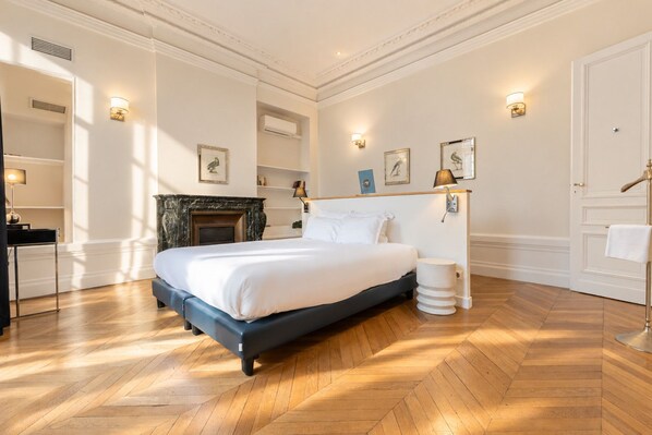 A bedroom with a large bed, a fireplace, a bedside table, and wall-mounted lamps. - Maison Ingwë - Appartment for 6 in Place Gambetta (Bordeaux)