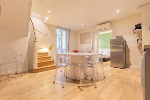 A modern kitchen with a dining area, wooden staircase, and a large window.