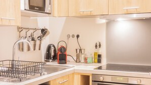 A modern kitchen with wooden cabinets, a built-in microwave, a kettle, a coffee maker, a dishwasher, and an oven.