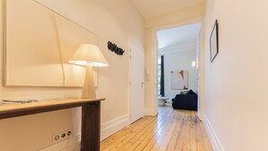 A hallway with a wooden floor, a desk with a lamp, a door, and a dark-colored sofa in the background.
