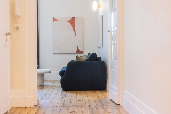 A hallway with a wooden floor, a white door, a blue sofa, and a wall-mounted artwork.