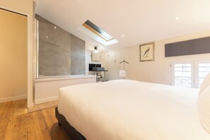 A modern hotel room with a large bed, a bathroom with a shower, a small desk, and a window with a view.