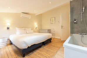 A bedroom with a bed, bedside tables, a nightstand, an air conditioner, a shower, and a door.