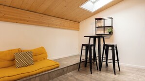 A room with a wooden ceiling, a yellow sofa with a patterned pillow, and a black table with two stools.