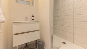 A bathroom with a white vanity, a mirror, a bottle of soap, and a shower with textured tiles.