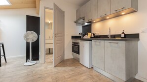 A compact kitchen with a built-in oven, a small refrigerator, and a countertop with a kettle and toaster.