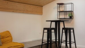 A room with a wooden ceiling, a skylight, a black metal shelf with items, two black stools, and a mustard-colored sofa.