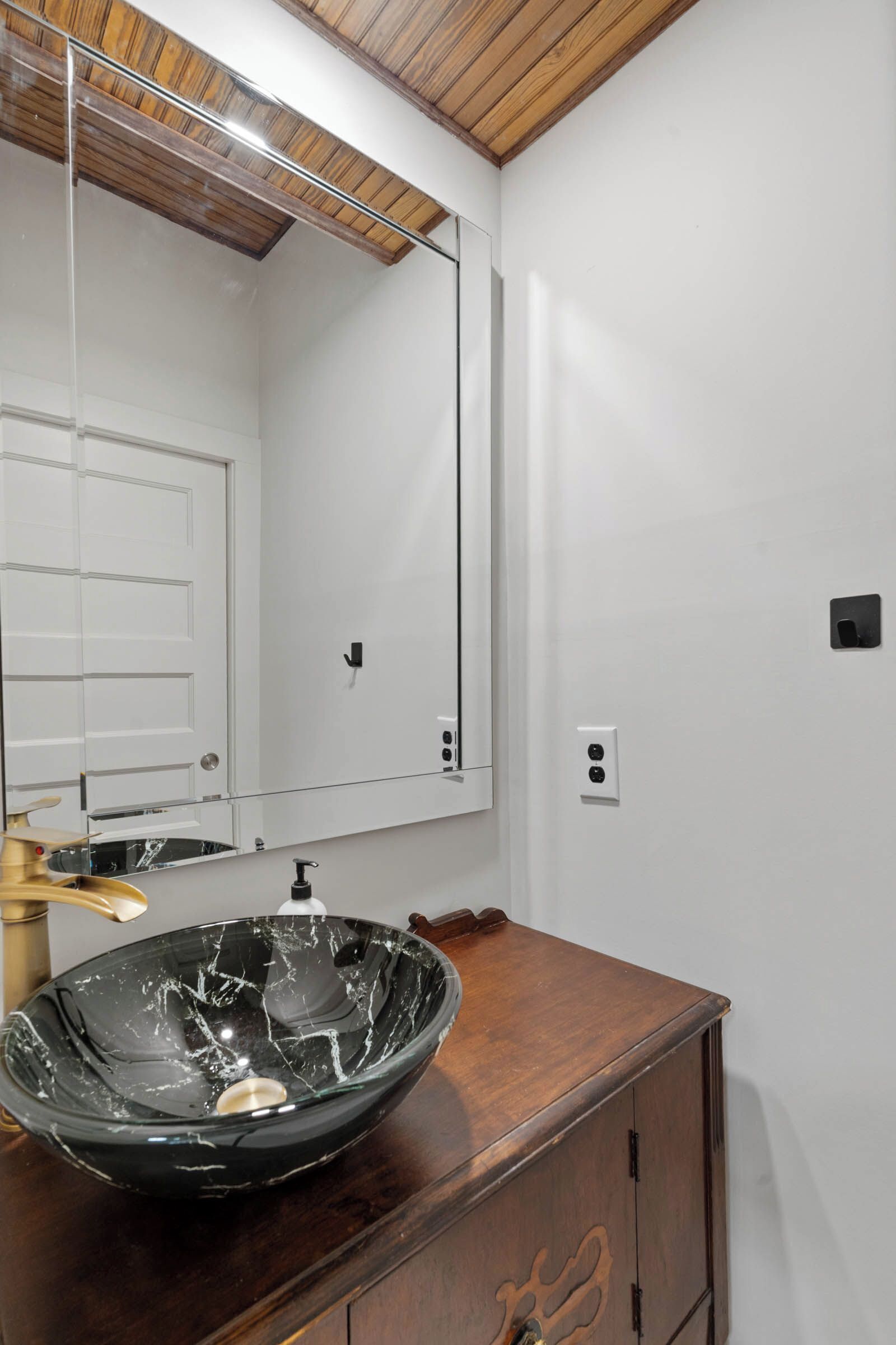 A bathroom with a wooden vanity, a glass bowl sink, a mirror, and a white door.