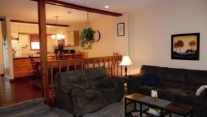A living room with a sofa, a coffee table, and a lamp. There is a dining area with a table and chairs in the background. - Poconos Dream House (East Stroudsburg)